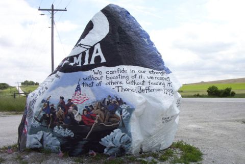 1981 Ford Bronco - A large rock painted with patriotic imagery and quotes sits by a roadside under a utility pole.
