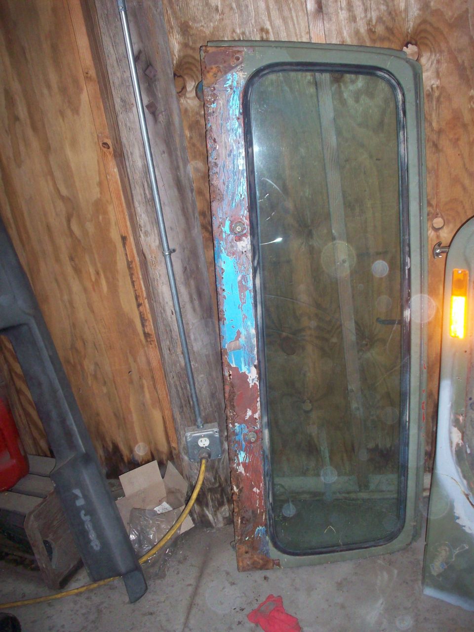 Jeep door with peeling blue and red paint over rust, and a green-tinted window