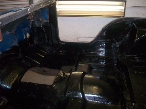 1978 Jeep CJ5 - The interior floor of a vehicle is coated in black paint, revealing structural elements and some padding.