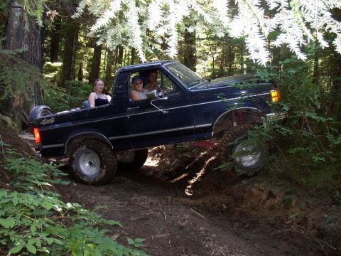 1988 Ford Bronco driving off-road with three people inside