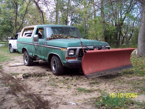 1979 Ford Bronco - This green Ford Bronco is equipped with a snow plow and parked next to another vehicle.