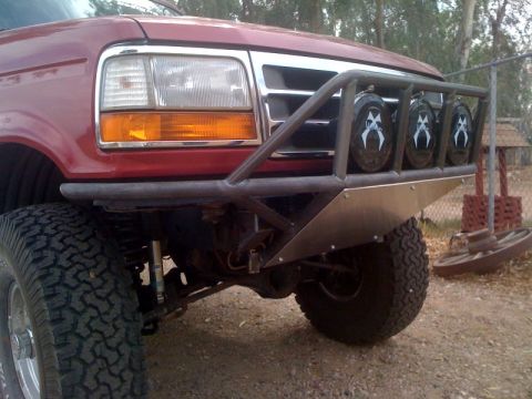 1989 Ford Bronco - This red Ford Bronco features a custom front bumper with auxiliary lights and off-road tires.