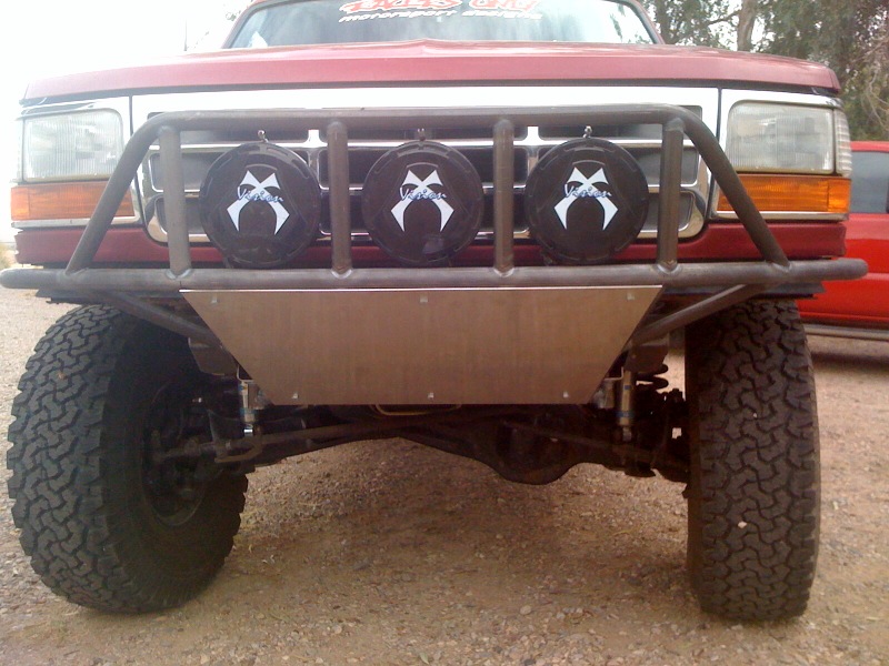 Red Ford truck front view with custom metal bumper, three lights, and off-road tires