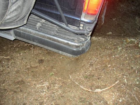 1988 Ford Bronco - The rear corner of a dark SUV is visible, with a spare tire mounted above the bumper.
