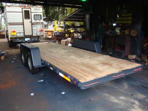 1988 Ford F-350 - A car hauler trailer is parked under a covered area, with a camper on a truck behind it.