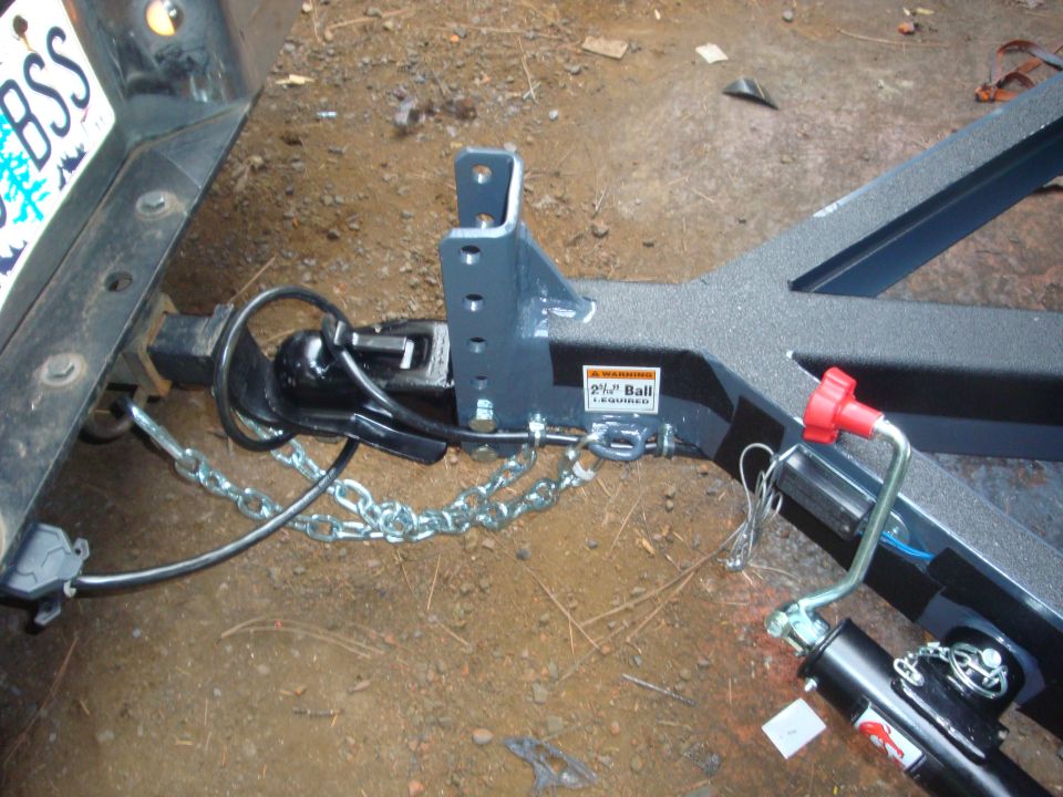 Trailer hitch assembly with coupler, safety chains, and wiring connector attached to a vehicle's receiver. A warning sticker indicates a 2-inch ball is required
