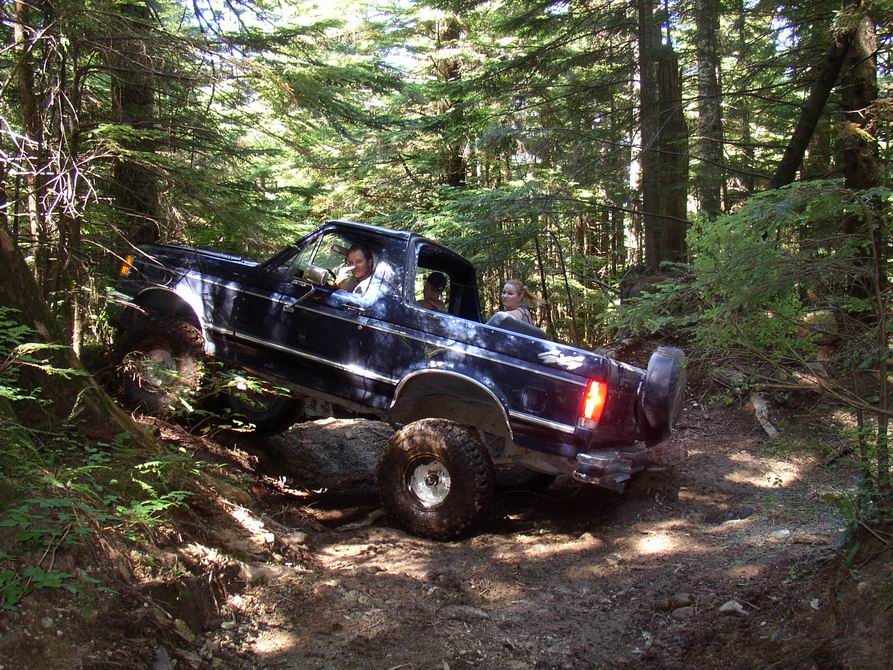 Dark blue Ford Bronco off-roading on a rocky, wooded trail