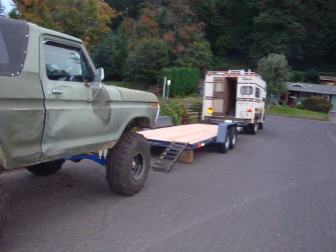 1988 Ford F-350 - Olive green Ford Bronco tows a flatbed trailer with a camper attached.