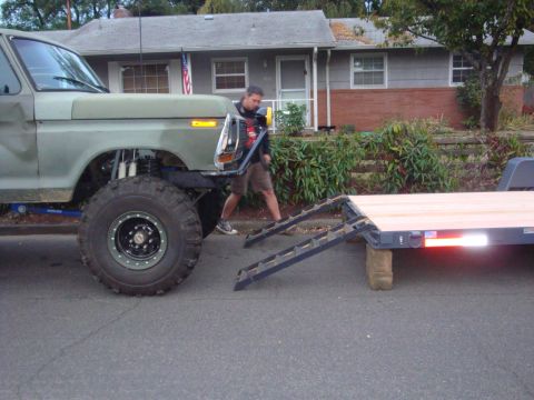 1988 Ford F-350 - A heavily modified pickup truck is positioned next to a flatbed trailer with ramps.