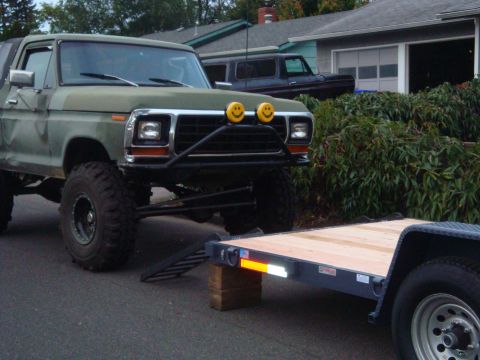 1988 Ford F-350 - This lifted Ford Bronco features smiley face auxiliary lights and is positioned next to a utility trailer.