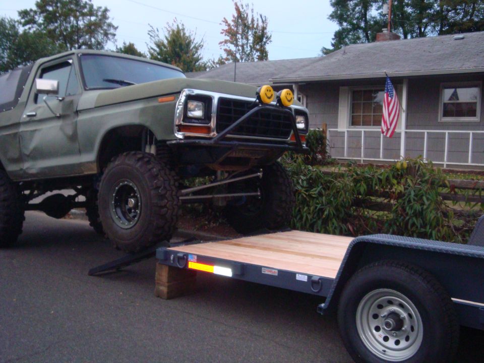 Lifted 1978 Ford Bronco with custom bumper and smiley face lights is being loaded onto a flatbed trailer