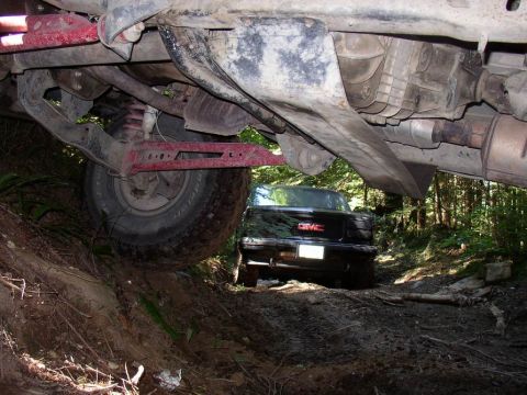 1988 Ford Bronco - A black GMC pickup truck is visible on a dirt path, viewed from beneath the chassis of another off-road vehicle.