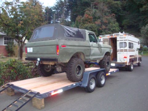 1988 Ford F-350 - A lifted Ford Bronco is loaded onto a trailer, with a pickup truck carrying a camper shell behind it.