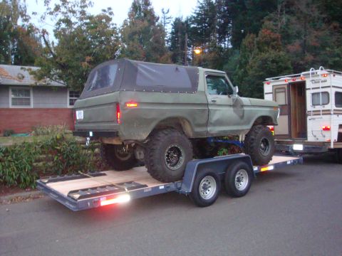 1988 Ford F-350 - A lifted Ford Bronco is transported on a trailer, with a camper hitched behind it.