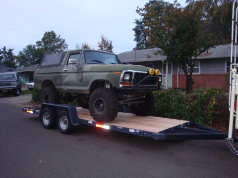 1988 Ford F-350 - A lifted, green Ford Bronco with a soft top is loaded onto a trailer.
