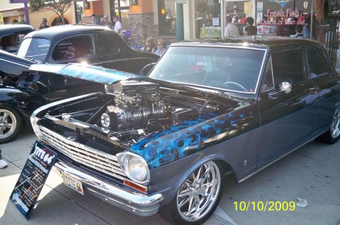 1985 Ford Bronco - A customized 1964 Chevrolet Nova SS is displayed with its hood open, revealing a powerful engine and custom paint.