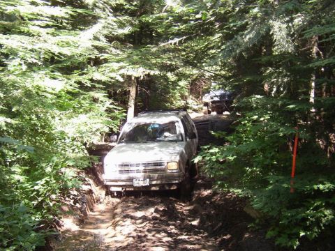 1988 Ford Bronco - Vehicles navigate a challenging, muddy path through a dense forest.