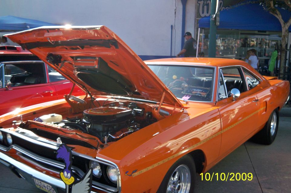 Orange 1970 Plymouth Road Runner with hood open, showing engine. A red car is partially visible to the left