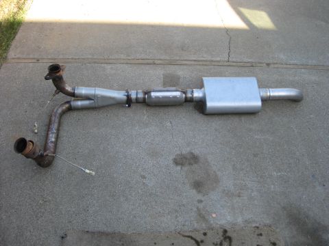 1995 Ford Bronco - Exhaust system part, likely a Y-pipe and muffler assembly, laid out on concrete.