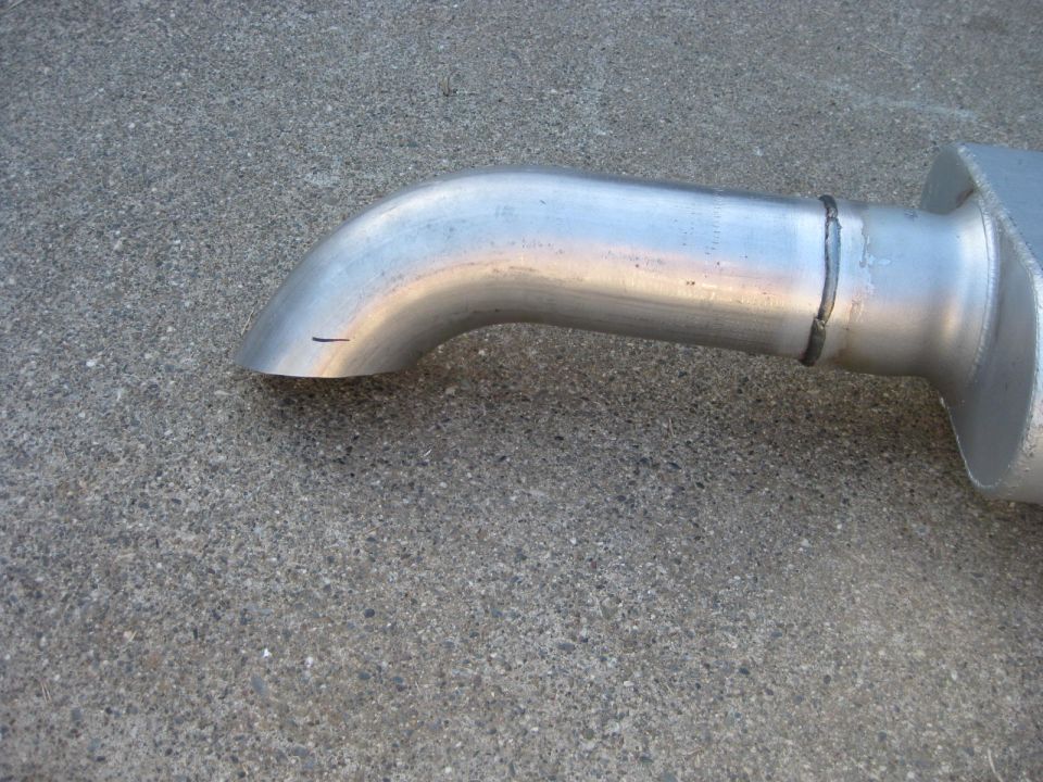Exhaust pipe with a bend leading to a muffler, resting on concrete