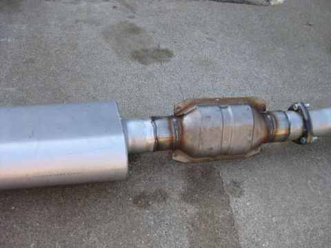 1995 Ford Bronco - A freshly fabricated stainless exhaust assembly lying on concrete: an oval muffler welded to a short pipe, a round catalytic converter with…