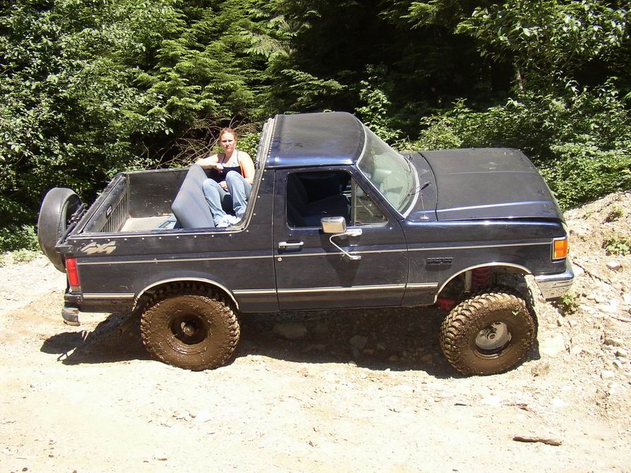 Dark blue 1987 Ford Bronco with off-road tires and a woman in the bed