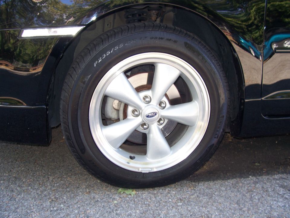 Close-up of a silver 5-spoke wheel with a Ford logo on a black car's tire