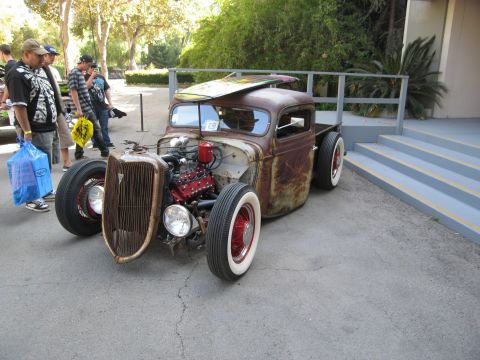 1986 Ford Bronco - Rat rod pickup truck with a surfboard on its roof, displayed outdoors.