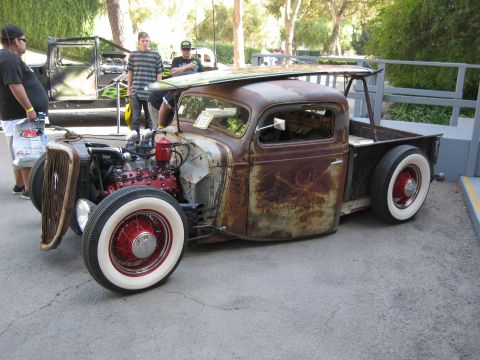 1986 Ford Bronco - A heavily customized rat rod pickup truck is displayed outdoors with a surfboard secured to its roof.