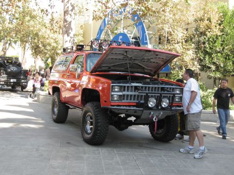 1986 Ford Bronco - An orange SUV with its hood open is displayed at an outdoor event, with people observing.