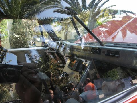 1986 Ford Bronco - View from inside a vehicle, showing the dashboard and reflections of palm trees and people in the windshield.