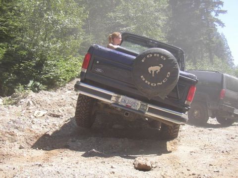 1988 Ford Bronco - A blue Ford Bronco navigates a rough, dusty trail with another dark SUV following behind.