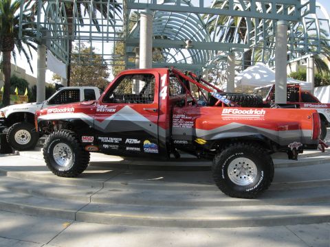 1986 Ford Bronco - A modified red off-road truck is parked next to a white truck at an outdoor event.