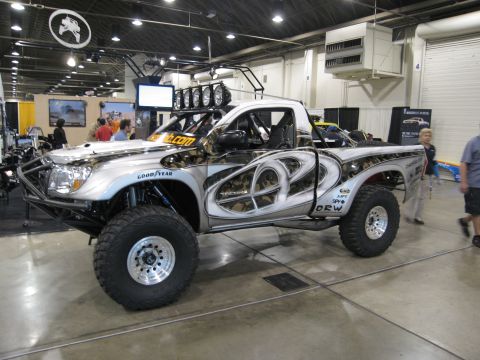 1986 Ford Bronco - A heavily modified pickup truck with custom paint and off-road tires is displayed at an expo.