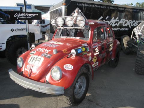 1986 Ford Bronco - A modified red Volkswagen Beetle is parked next to a trailer and other off-road vehicles.