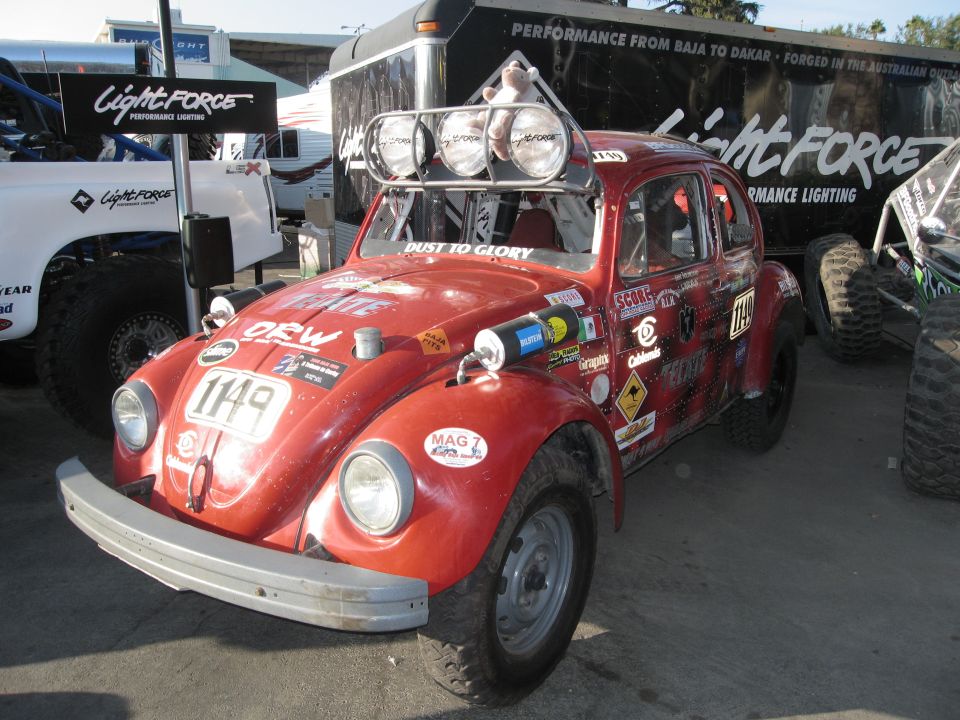 Red Volkswagen Beetle with off-road tires, light bar, and numerous stickers