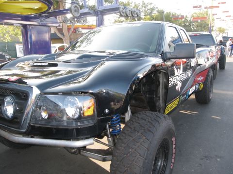 1986 Ford Bronco - A modified black truck with extensive off-road modifications is seen at an event, with another vehicle visible behind it.
