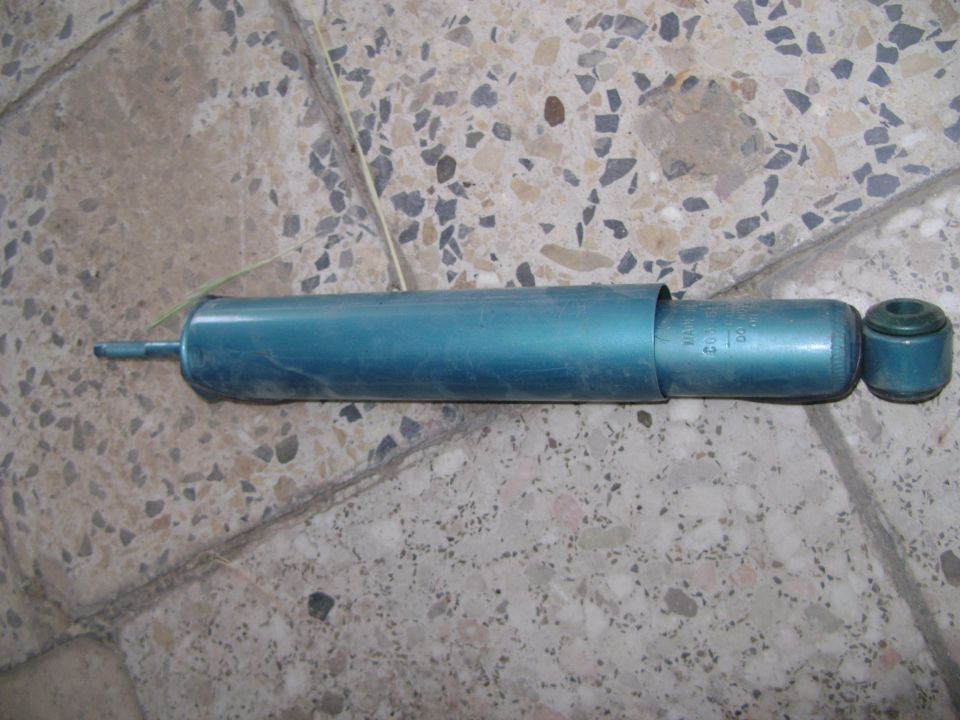 Teal shock absorber with a rubber bushing on the end, lying on a terrazzo floor