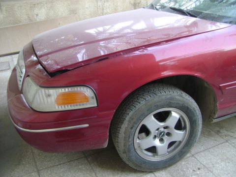 1998 Ford Crown Victoria - The front fender and headlight assembly of a red 1998 Ford Crown Victoria are visible, with the hood open.