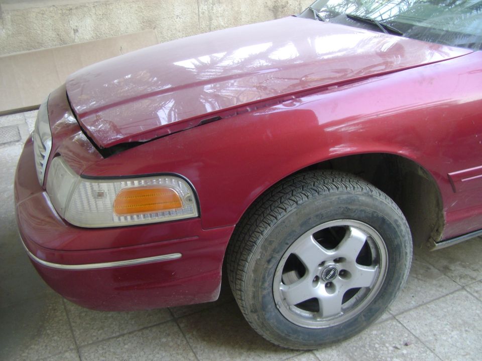 Front corner of a red 1998 Ford Crown Victoria. Hood is slightly ajar