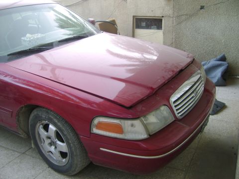 1998 Ford Crown Victoria - The front driver's side of a red 1998 Ford Crown Victoria is shown, with the hood slightly ajar.