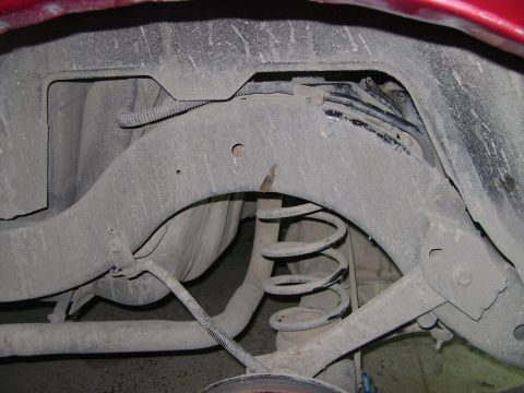 1998 Ford Crown Victoria - The rear suspension system of a vehicle is visible, with a focus on the coil spring and associated metal components.