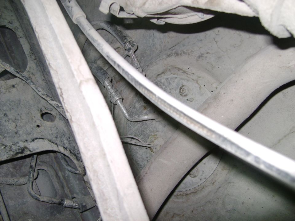 Undercarriage of a vehicle showing suspension components and exhaust pipe. Dusty and worn