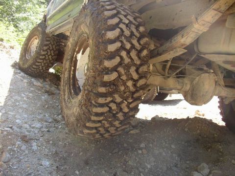 1988 Ford Bronco - The underside of a vehicle with large, mud-caked tires navigating a rough, gravelly path.