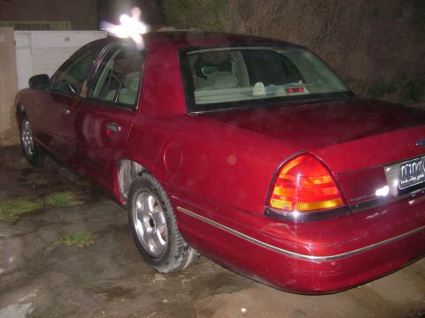 1998 Ford Crown Victoria - The rear of a red sedan is shown parked at night, with a license plate visible.