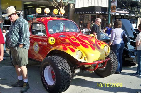 1985 Ford Bronco - Customized Volkswagen Beetle with flame graphics and off-road tires on display.