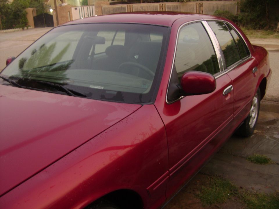 Red 1998 Ford Crown Victoria, front quarter panel and driver's side visible, wet surface