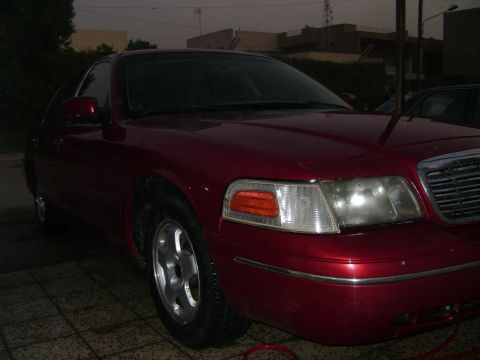 1998 Ford Crown Victoria - This red sedan is shown from the front quarter angle, highlighting its headlights and grille.