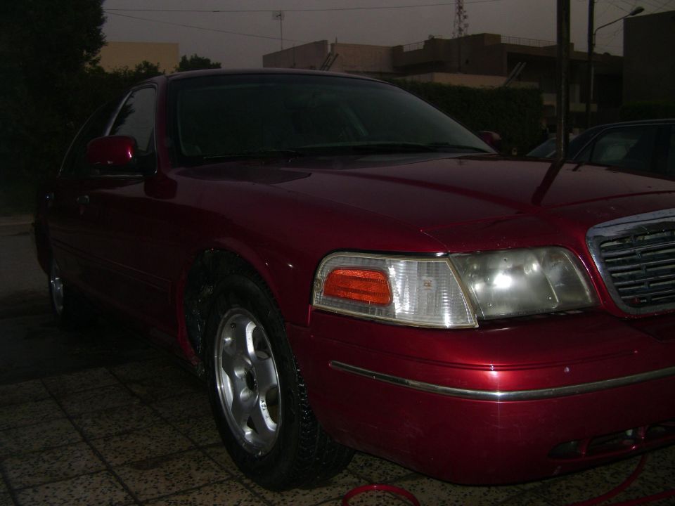 Red sedan, front quarter view. Shows headlights, grille, and side mirror