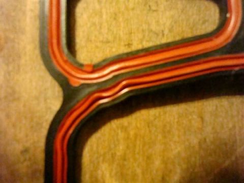 1998 Ford Crown Victoria - Close-up of a plastic intake manifold gasket with red sealing material, likely for an automotive engine.